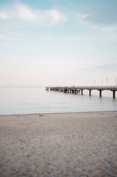 Ruhiger Strand mit einem Holzsteg, sanfte Wellen und ein klarer Himmel.