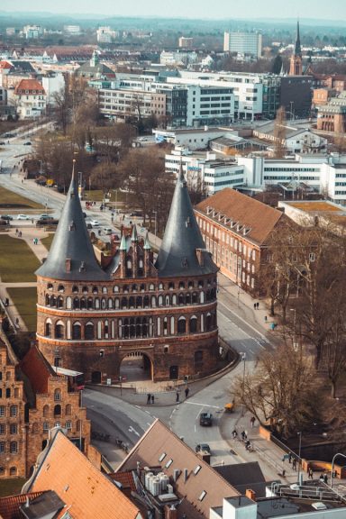 Historisches Gebäude mit zwei Türmen, umgeben von modernen Stadtstrukturen und Grünflächen.