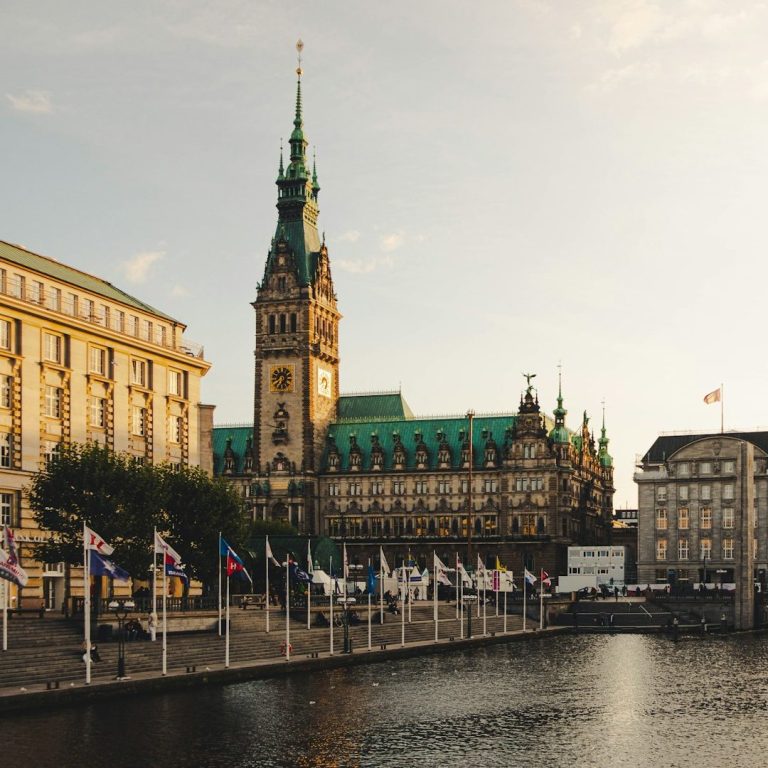 Historisches Gebäude mit Uhrturm und Flaggen am Wasser in Hamburg.