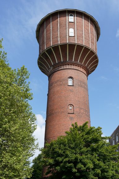 Ziegender, roter Wasserturm umgeben von Bäumen und klarem Himmel.