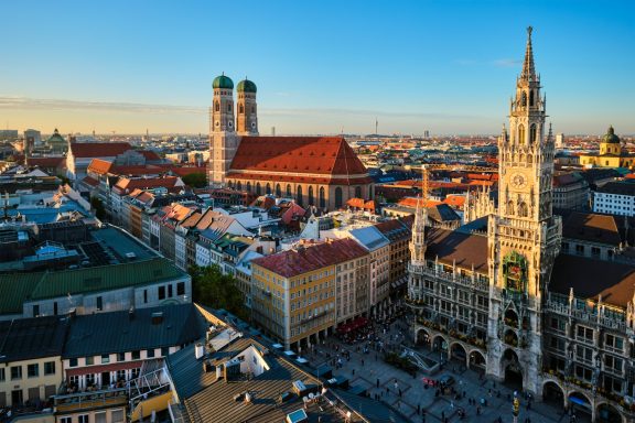 Blick auf München mit der Frauenkirche und dem Neuen Rathaus bei Sonnenuntergang.