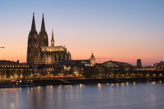 Kölner Dom bei Sonnenuntergang, beleuchtet am Rheinufer.