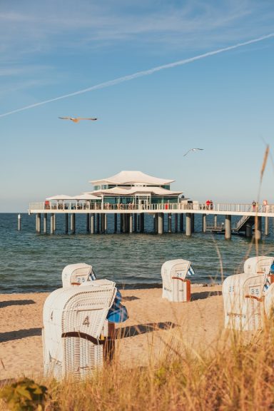 Blick auf einen Steg mit Möbeln am Strand und einem klaren blauen Himmel.