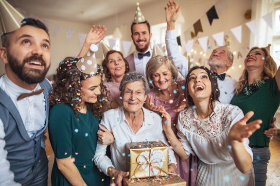 Gruppenfoto von feiernden Menschen mit Geschenken und Konfetti in fröhlicher Atmosphäre.