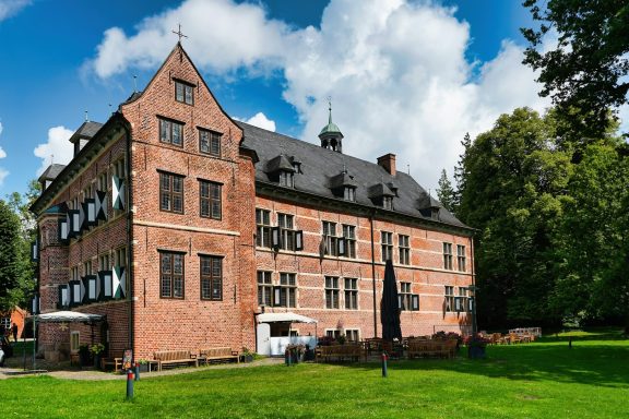 Historisches Gebäude mit roten Ziegeln, grüner Wiese und wolkigem Himmel.