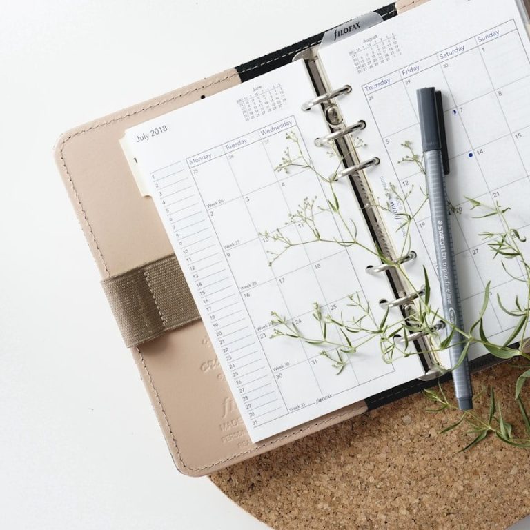 Kalender mit einem Stift und einem Zweig auf einem Korkunterlage.